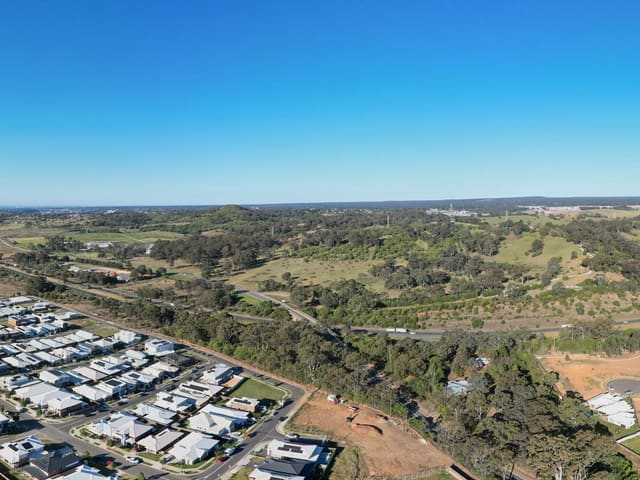 Over the finished streets on the north-east side of Menangle Road, above the park at the top of Mount Pleasant Drive — the developer's name for it is Hilltop Park; Council does not list it. Past the park, large buildings are going up on fresh slabs. Nothing published yet says what they will be.