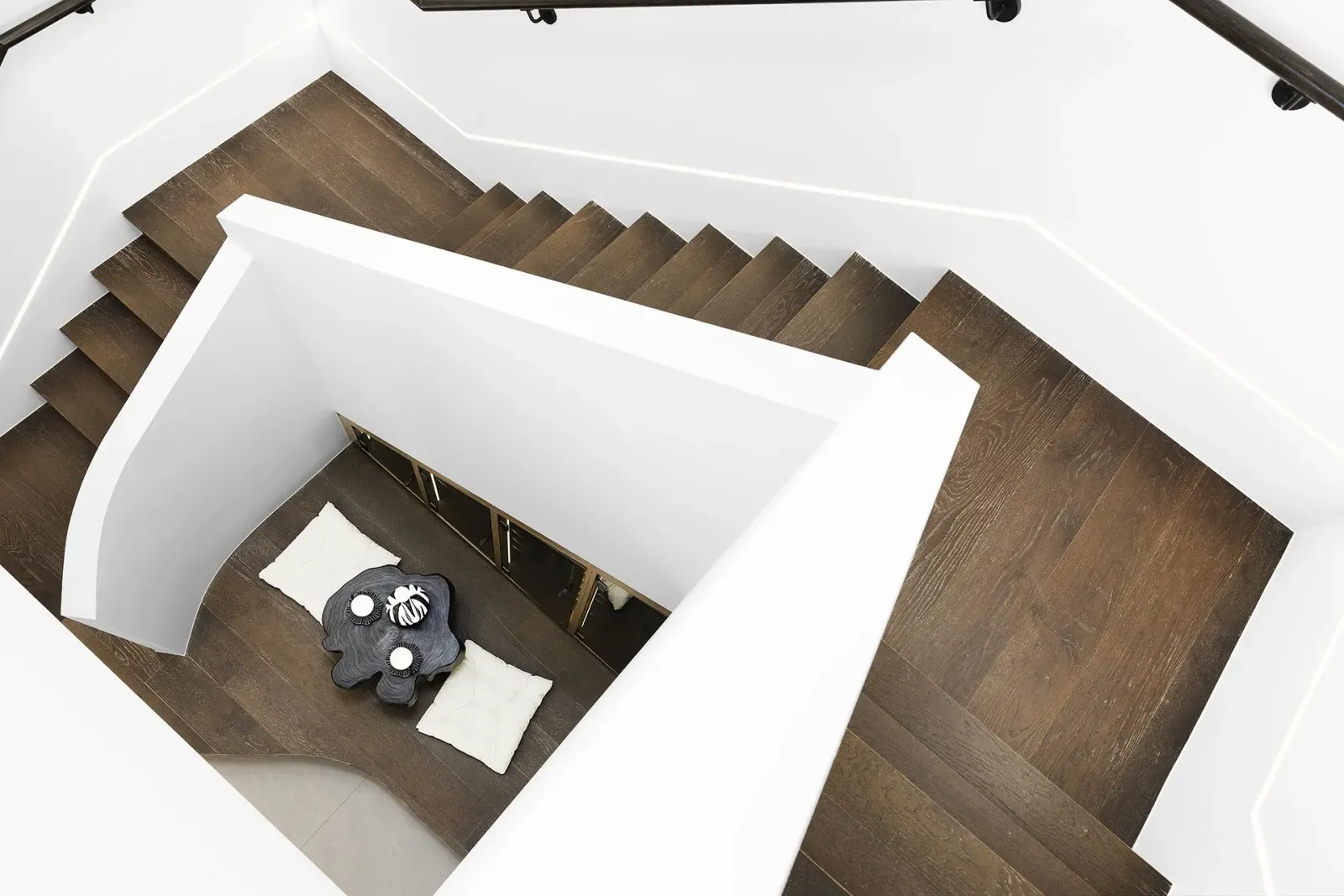 A timber staircase photographed straight down from the landing, turning around a white balustrade to the floor below.
