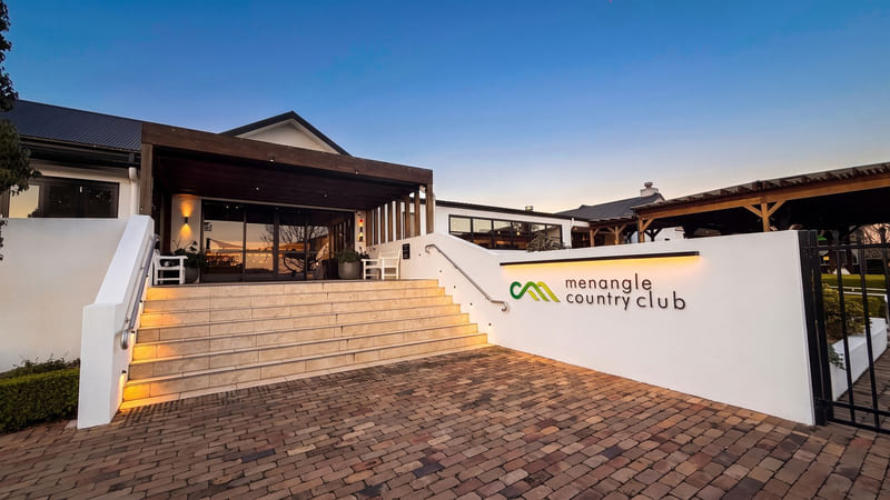 Brick paving and steps leading up to a modern clubhouse entrance with a covered terrace.