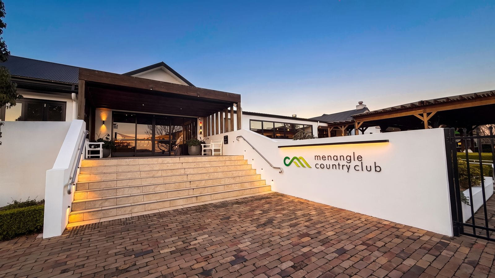 Brick paving and steps leading up to a modern clubhouse entrance with a covered terrace.