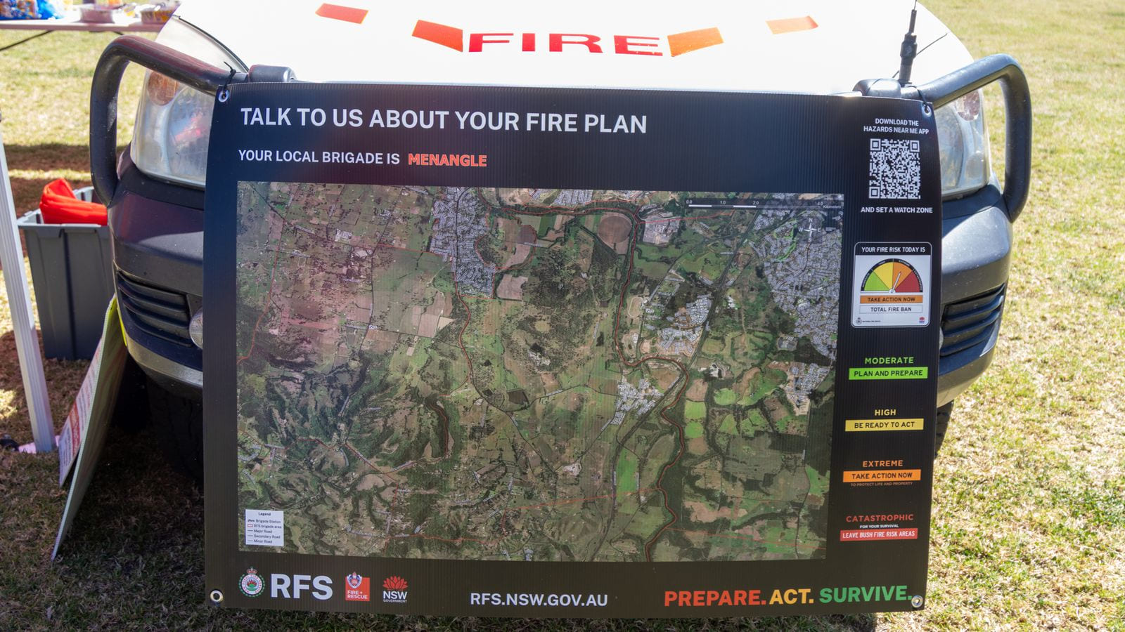 A black RFS board leaning against the front of a vehicle, showing an aerial map outlined in red beside a column of fire danger ratings from moderate to catastrophic.