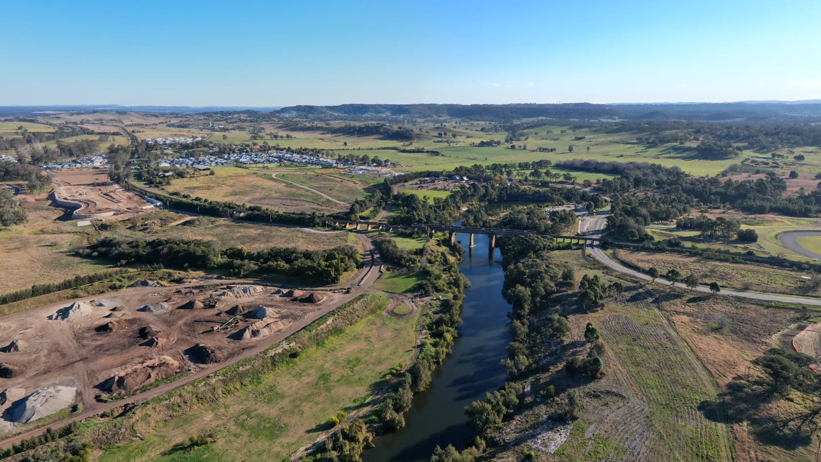 Aerial view of a river winding between wooded banks, with quarry workings on one side and a bridge downstream.