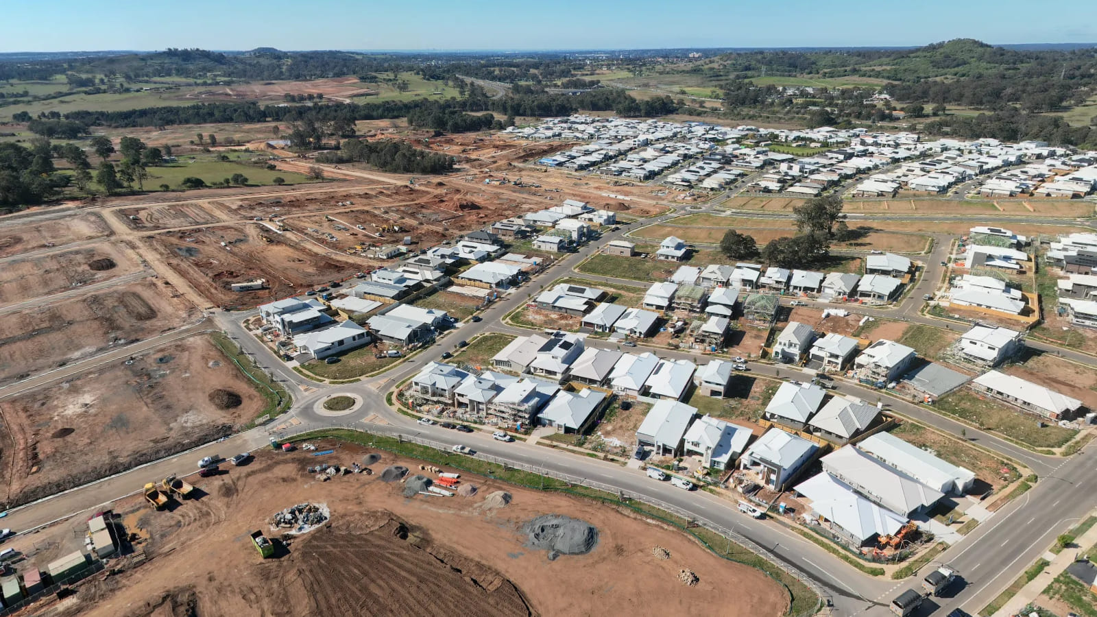 Aerial view of new houses on suburban streets with excavators and bare earth immediately beside them.