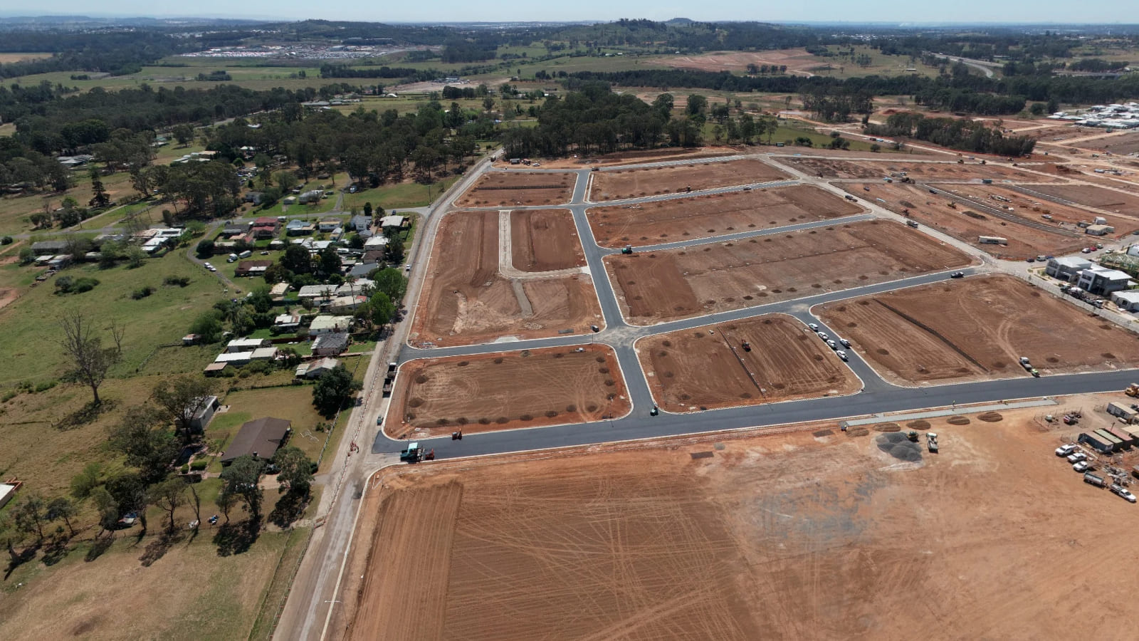 Dark surfaced roads forming a street grid through bare ground, with houses alongside.