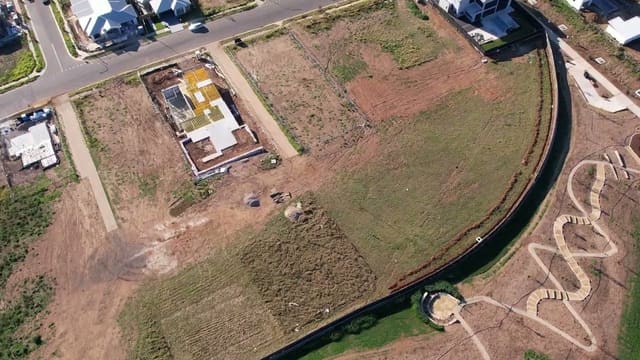 Lower, and looking straight down — finished streets, a house going up on its slab, vacant lots waiting, and the formed paths of a new reserve at the estate's edge.
